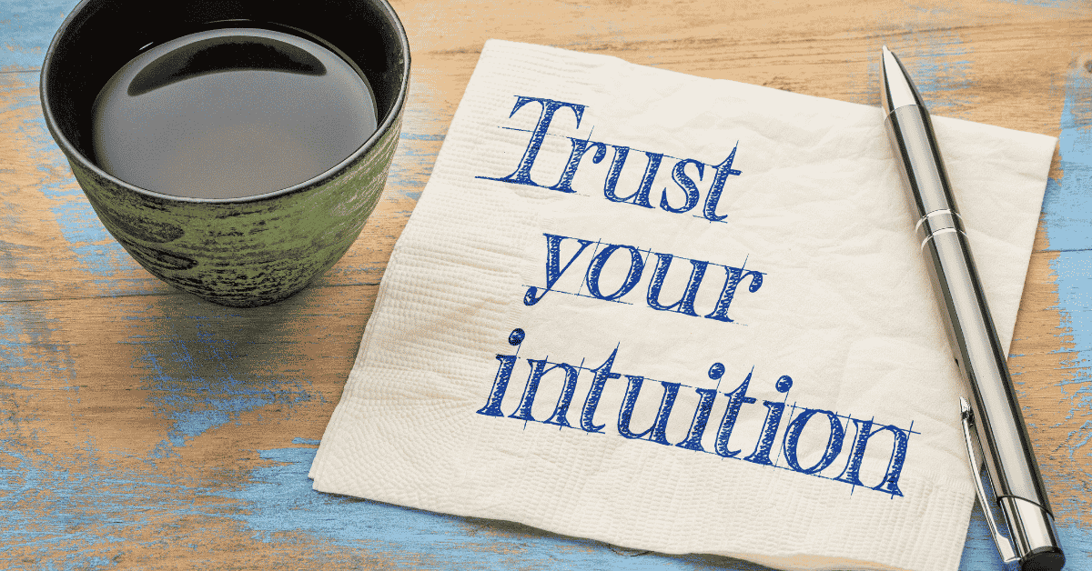 A napkin that says in blue writing "trust your intuition" on a table with a pen and cup of tea