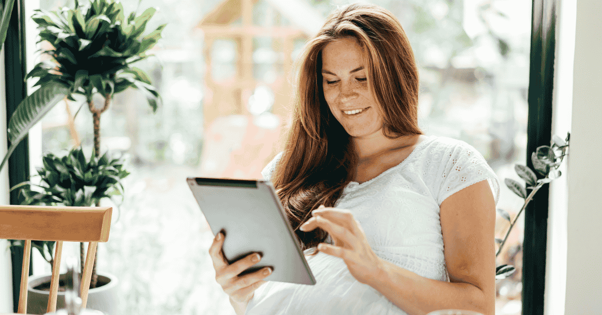 A woman holding a tablet smiling joyfully surrounded by plants symbolizing her protecting her peace on social media