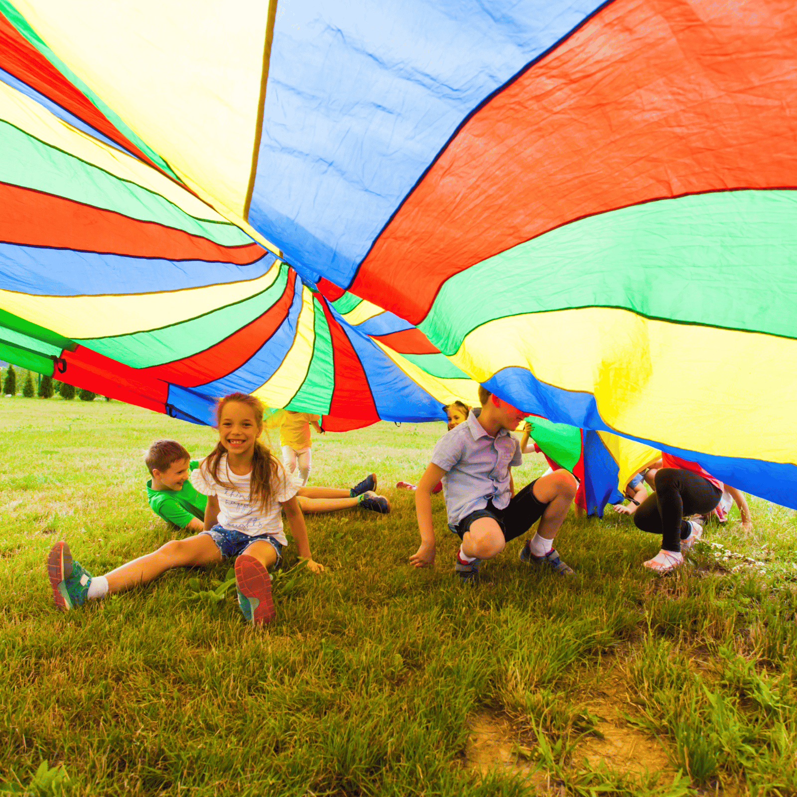 Kids playing underneath a rainbow parachute