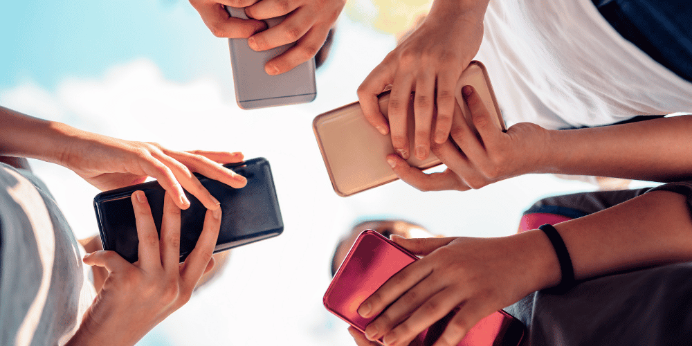 An image showing four people holding phones with the focus on the phones with a blue sky behind them
