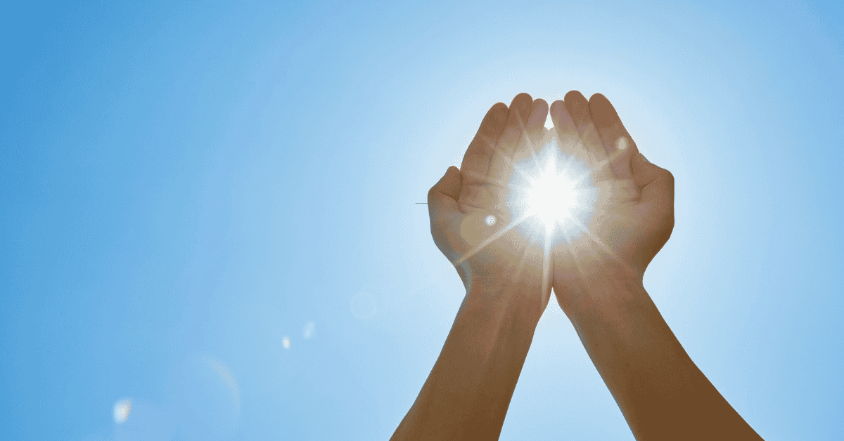 a blue sky with hands cupped capturing the sunshine which is illuminated like a balll of energy with rays outpouring on all sides refelection our shared experiences with energy 