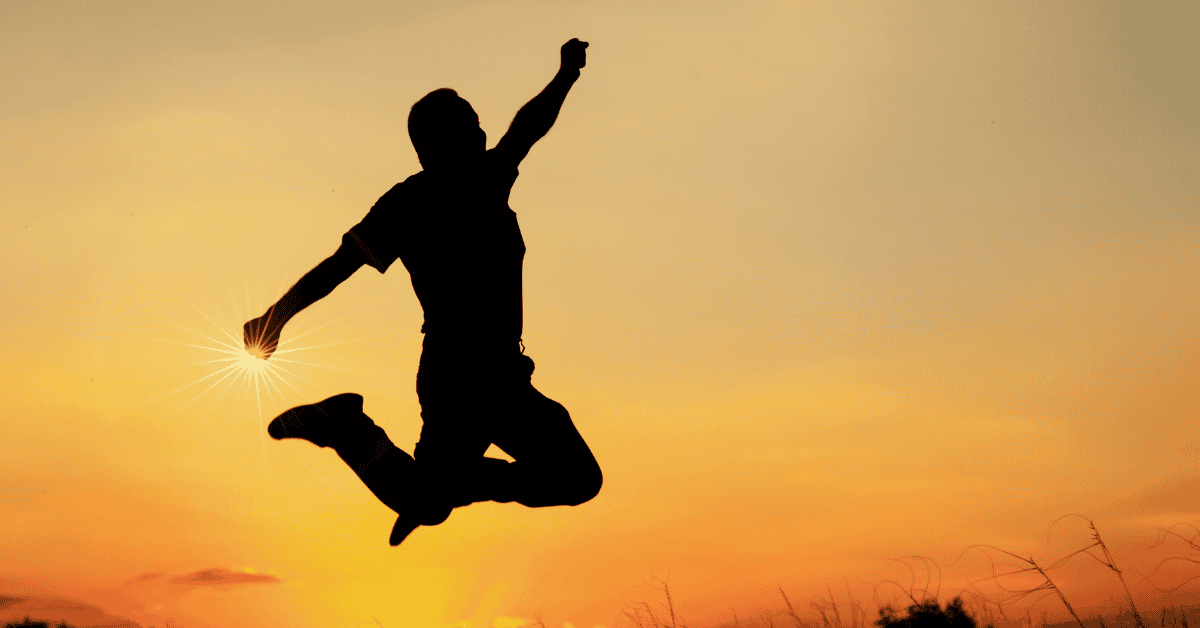 a dark silhouette of someone jumping for joy with the sky in the background at sunset